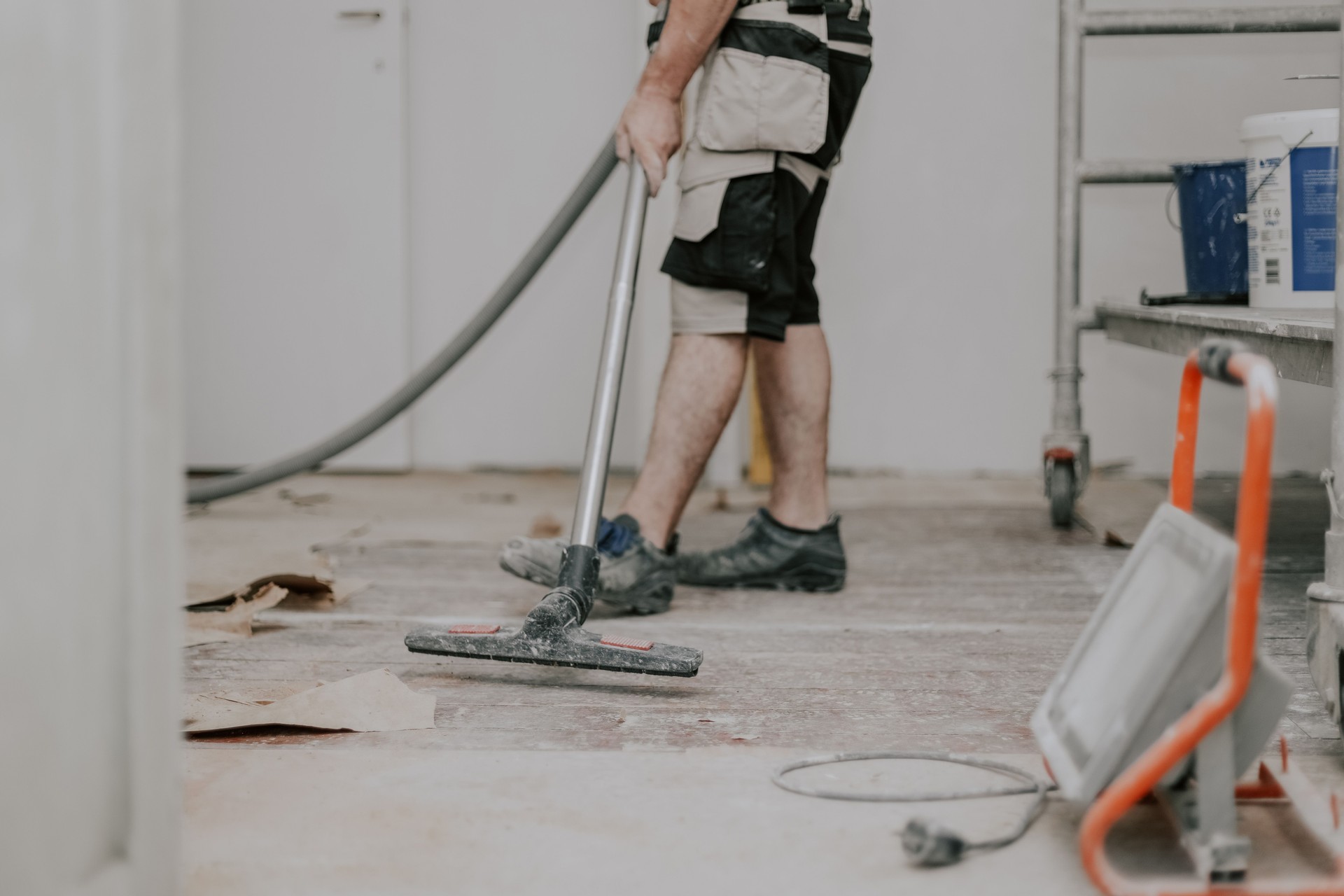A young man vacuums the floor with a construction vacuum cleaner.